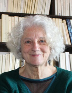 Monique Chignier posant devant une bibliothèque de livres derrière elle.