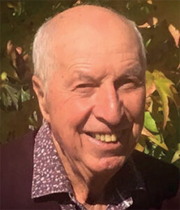 Photo de Jean-Jacques Couasnon portant une chemise violette devant un arbuste feuillu.