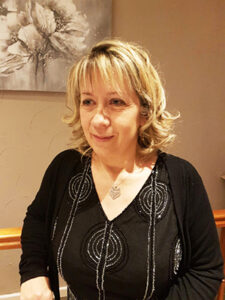 Visuel représentant l'auteure Sandrine Peyrard avec une robe noire sur un fond marron clair et un tableau accroché au mur.